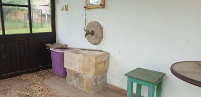 Stone sink with wall-mounted faucet on veranda next to a broom and purple laundry basket
