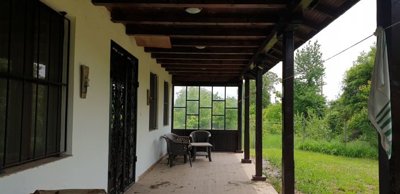 Covered veranda featuring wooden beams, plastic chairs, and a view of the garden