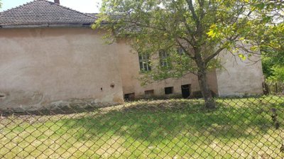 Beige old school building with barred windows and large tree in fenced grassy yard