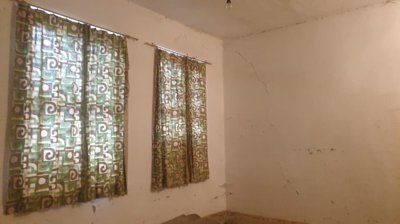 Room inside the building featuring two windows with green patterned curtains and cracked walls
