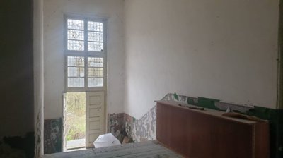 Hallway inside the building featuring a tall window and door opening to the outside, with worn walls and floor