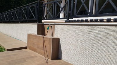 Water tap installed on terrace wall with tiled floor surrounding