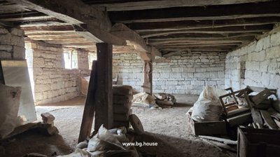 Spacious stone basement room featuring exposed wooden beams and various construction materials scattered on the dirt floor.