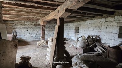 Interior view of a stone basement showing wooden support beams and piles of construction debris on the floor.