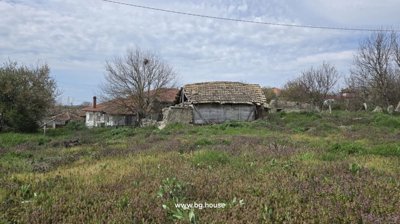 Exterior view of a traditional Bulgarian house showing stone basement, wooden balcony, and tiled roof under a clear sky.