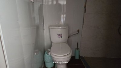 White toilet with a small trash bin and toilet brush in a tiled bathroom corner