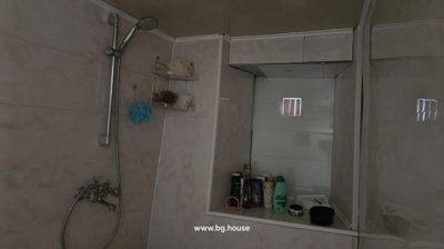 Shower area with wall-mounted showerhead and shelf holding bath sponges and toiletries