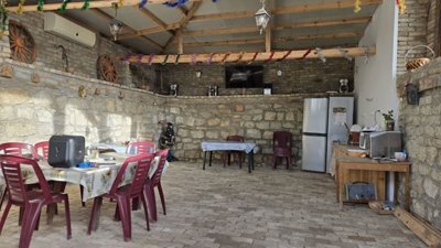 Outdoor covered dining area with stone walls, plastic chairs, tables, and decorative wooden wheels