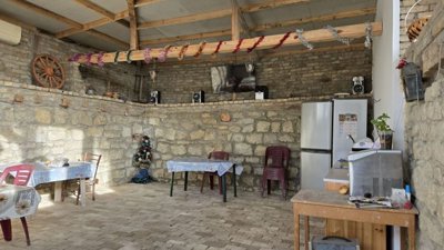 Outdoor kitchen and entertainment space with stone walls, refrigerator, TV, and plastic chairs