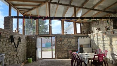 Wide view of the covered dining area featuring stone walls, tables, chairs, and decorative elements