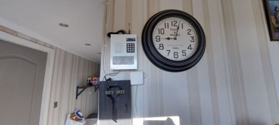 Interior wall featuring a large round clock, an intercom system, and a key box against striped wallpaper.