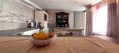 View of the kitchen showing tiled walls, a kitchen island with built-in oven, and a decorative fruit basket on the counter.