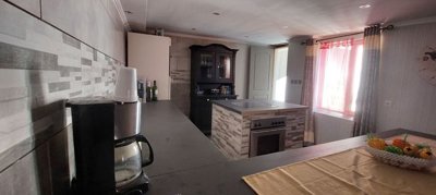 Kitchen area featuring tiled walls, a kitchen island with built-in oven, and a window dressed with pink curtains.