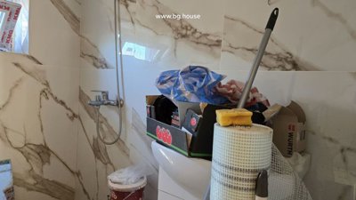 Bathroom shower area showing a wall-mounted shower faucet and cleaning supplies placed on the toilet cistern