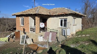 Side perspective of a Bulgarian rural house showing stone foundation and brick walls under clear blue sky