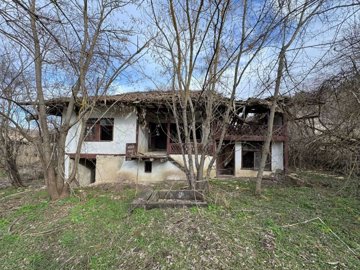Exterior view of an old house in Balkanski village showing white walls, wooden balcony, and surrounding bare trees.