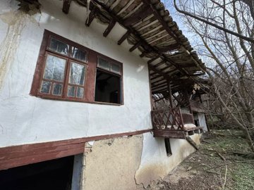 Close-up showing white plaster wall, window, wooden balcony, and basement entrance of the old house.