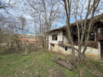 Side perspective of the old house showing white plaster walls, wooden balcony, and surrounding bare trees.