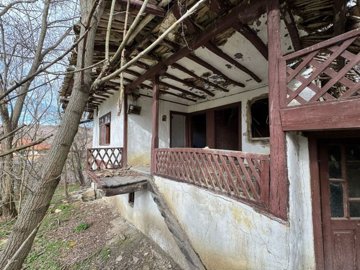 Close-up showing wooden balcony with peeling paint and entrance door of the old house surrounded by leafless trees.