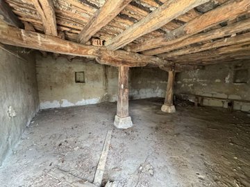Interior view of the basement showing wooden support beams and bare concrete floor with unfinished walls.
