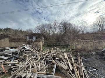 Wide garden view showing piles of wooden debris and old mud brick walls surrounding the property.