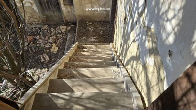 View looking down a wooden staircase outside, adjacent to a wall with peeling plaster and debris on the ground.