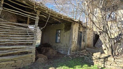 Wooden hay storage structure filled with hay next to a rural house, surrounded by bare trees.