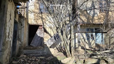 Entrance area of a rural house showing stone steps, wooden doors, and bare trees casting shadows.