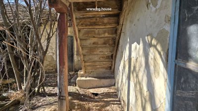 Wooden staircase attached to the exterior wall of a rural house with peeling plaster and bare trees nearby.