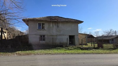 Front view of a two-storey rural house with plastered walls and tiled roof beside a road