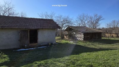 Two-storey rural house with plastered walls and tiled roof in grassy yard with old stone buildings