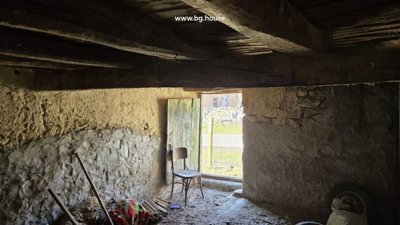 Interior view of a rustic room with exposed wooden beams and an open door leading outside.