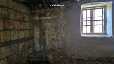 Interior view of a room with a barred window and walls made of stone and bricks.