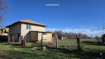 Rural house with fenced yard and brick outbuilding surrounded by grass and leafless trees