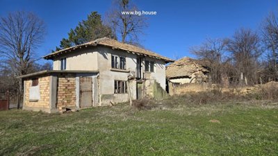 Two-storey rural house with plastered walls and tiled roof beside fenced grassy yard