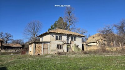 Two-storey rural house with plastered walls and tiled roof in grassy yard with old stone building