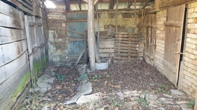 Inside view of a rustic barn showing wooden doors, stacked crates, and a dirt floor covered with leaves.
