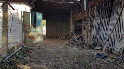 Open metal gate leading into a barn area with wooden slat walls and scattered debris on the ground.