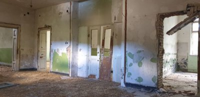Interior space showing damaged plaster walls, old doors, and straw covering the floor