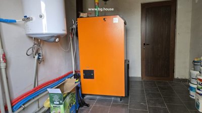 Orange heating unit with connected pipes and white water heater mounted on wall in tiled utility room