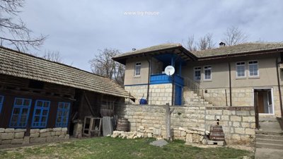 Side view of the Bulgarian house showing blue balcony, stone stairs, and wooden outbuilding