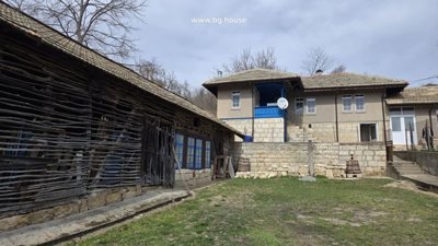 Rustic house with a wooden fence and stone wall enclosing a grassy yard area.