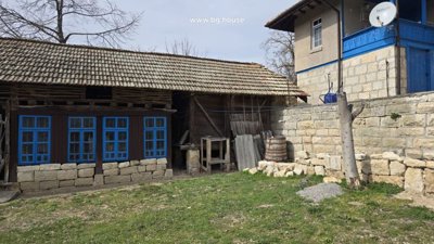 Stone base supporting a wooden fence with blue window frames beside the house.