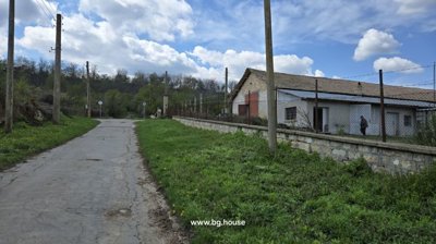 Road running alongside a stone wall and wire fence that encloses farm buildings and green land