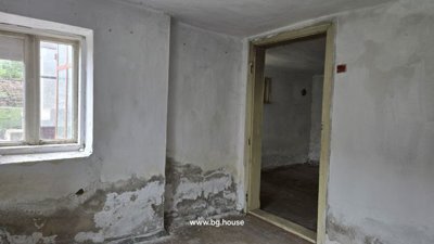 Indoor room showing white plastered walls, a window letting in natural light, and a door opening to an adjacent room