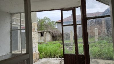 View from an indoor room through a window and door to an outdoor garden area with grass and old structures