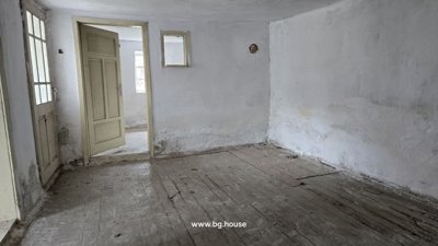Room with white painted walls, wooden floor, and door opening to another room