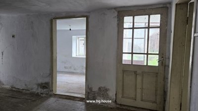 Room featuring a door, window, white walls, and wooden floorboards