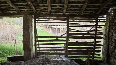 Looking through wooden slats of a rustic structure to a green garden area and a stone building beyond.