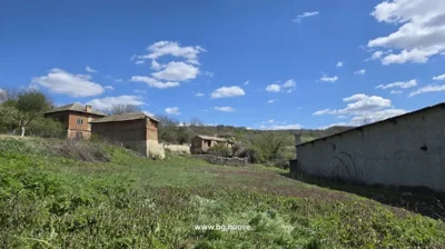 View of a green grassy field with trees and old brick buildings in the background under a blue sky with clouds.